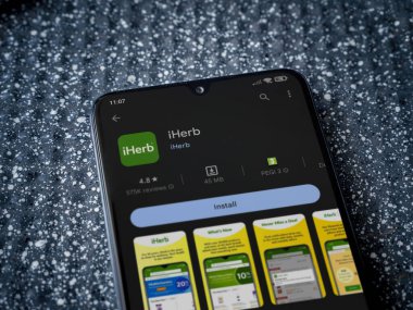Lod, Israel - July 16,2023: iHerb app play store page on the display of a black mobile smartphone on a metallic background. Close up top view flat lay.