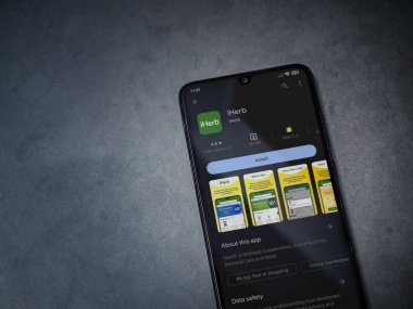 Lod, Israel - July 16,2023: iHerb app play store page on smartphone on a dark marble stone background. Top view flat lay with copy space.