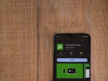 Lod, Israel - July 16,2023: Unified Remote app play store page on smartphone on wooden background. Top view flat lay with copy space.