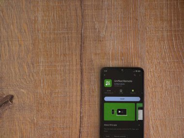 Lod, Israel - July 16,2023: Unified Remote app play store page on smartphone on wooden background. Top view flat lay with copy space.