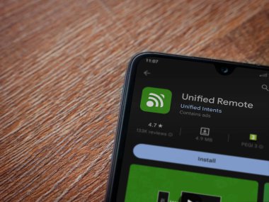 Lod, Israel - July 16,2023: Unified Remote app play store page on smartphone on wooden background. Top view flat lay with copy space.