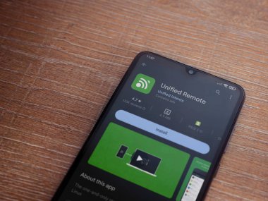 Lod, Israel - July 16,2023: Unified Remote app play store page on smartphone on wooden background. Top view flat lay with copy space.