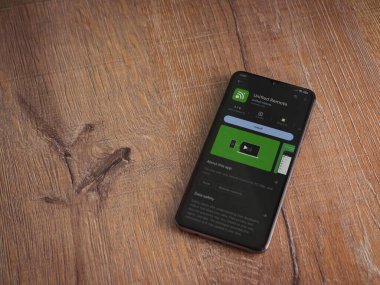 Lod, Israel - July 16,2023: Unified Remote app play store page on smartphone on wooden background. Top view flat lay with copy space.