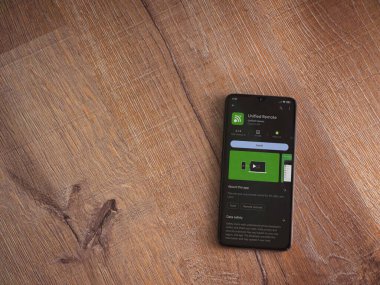 Lod, Israel - July 16,2023: Unified Remote app play store page on smartphone on wooden background. Top view flat lay with copy space.