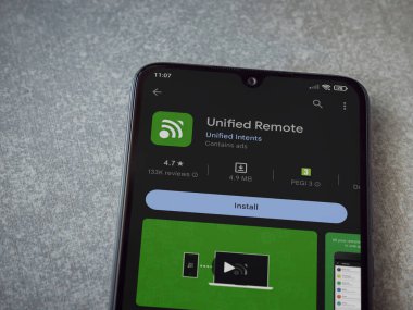 Lod, Israel - July 16,2023: Unified Remote app play store page on smartphone on ceramic stone background. Top view flat lay with copy space.