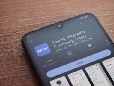 Lod, Israel - July 16,2023: Wear - Galaxy Wearable app play store page on smartphone on wooden background. Top view flat lay with copy space.