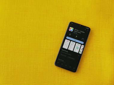 Lod, Israel - July 16,2023: Homey app play store page on smartphone on a yellow fabric background. Top view flat lay with copy space.