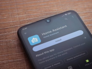 Lod, Israel - July 16,2023: Home Assistant app play store page on smartphone on wooden background. Top view flat lay with copy space.