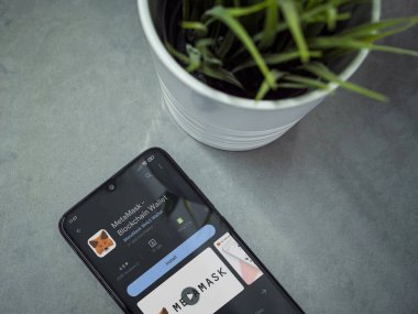 Lod, Israel - July 16,2023: Modern workspace with smartphone with MetaMask app play store page on marble background. Close up top view flat lay.