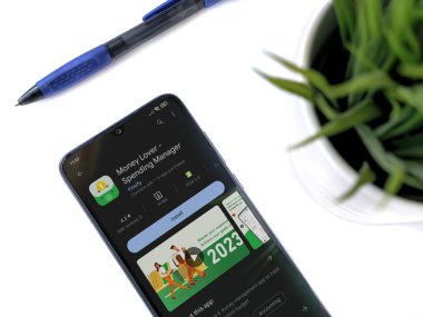 Lod, Israel - July 16,2023: Modern workspace with smartphone with Money Lover app play store page on white background. Close up top view flat lay.