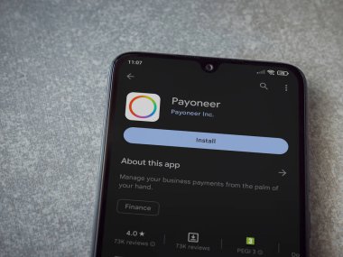 Lod, Israel - July 16,2023: Payoneer app play store page on smartphone on ceramic stone background. Top view flat lay with copy space.