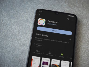 Lod, Israel - July 16,2023: Payoneer app play store page on smartphone on ceramic stone background. Top view flat lay with copy space.