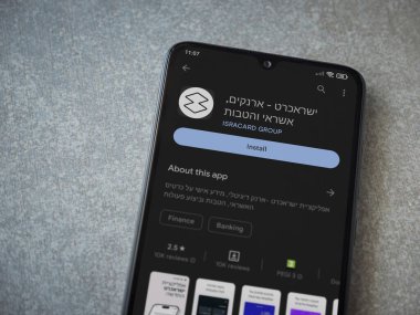Lod, Israel - July 16,2023: Isracard app play store page on smartphone on ceramic stone background. Top view flat lay with copy space.