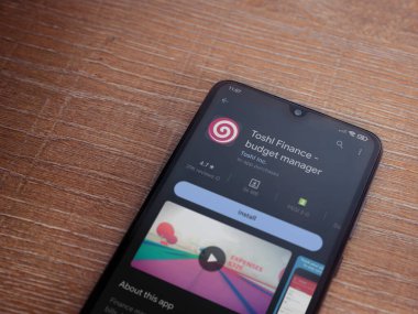 Lod, Israel - July 16,2023: Toshl Finance app play store page on smartphone on wooden background. Top view flat lay with copy space.