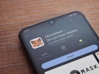 Lod, Israel - July 16,2023: MetaMask app play store page on smartphone on wooden background. Top view flat lay with copy space.