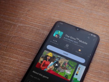 Lod, Israel - July 16,2023: The Sims Mobile app play store page on smartphone on wooden background. Top view flat lay with copy space.