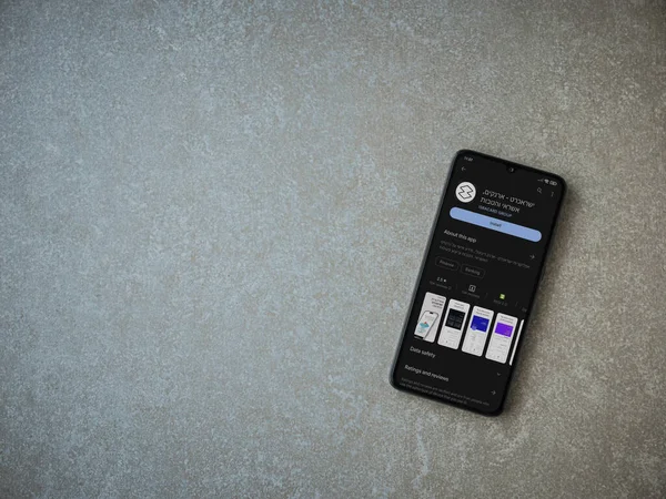 Lod, Israel - July 16,2023: Isracard app play store page on smartphone on ceramic stone background. Top view flat lay with copy space.