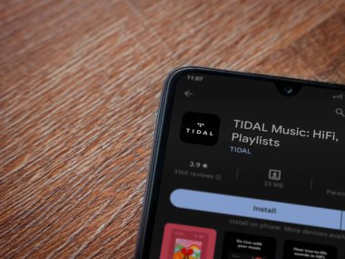 Lod, Israel - July 16,2023: TIDAL Music app play store page on smartphone on wooden background. Top view flat lay with copy space.