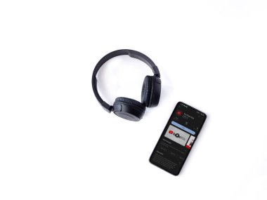 Lod, Israel - July 16,2023: Smartphone with YouTube Kids app play store page and wireless headphones on white background. Top view flat lay with copy space.