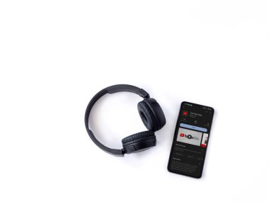 Lod, Israel - July 16,2023: Smartphone with YouTube Kids app play store page and wireless headphones on white background. Top view flat lay with copy space.
