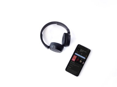 Lod, Israel - July 16,2023: Smartphone with TIDAL Music app play store page and wireless headphones on white background. Top view flat lay with copy space.