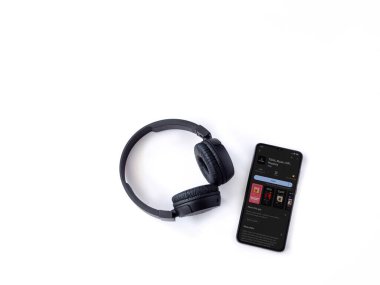 Lod, Israel - July 16,2023: Smartphone with TIDAL Music app play store page and wireless headphones on white background. Top view flat lay with copy space.