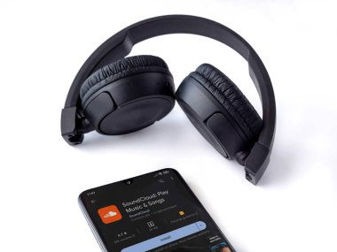 Lod, Israel - July 16,2023: Smartphone with SoundCloud app play store page and wireless headphones on white background. Top view flat lay with copy space.
