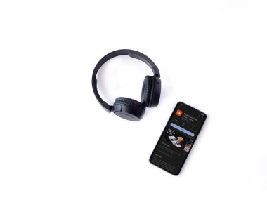 Lod, Israel - July 16,2023: Smartphone with SoundCloud app play store page and wireless headphones on white background. Top view flat lay with copy space.