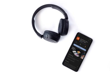 Lod, Israel - July 16,2023: Smartphone with SoundCloud app play store page and wireless headphones on white background. Top view flat lay with copy space.