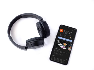 Lod, Israel - July 16,2023: Smartphone with SoundCloud app play store page and wireless headphones on white background. Top view flat lay with copy space.