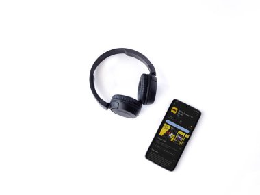 Lod, Israel - July 16,2023: Smartphone with IDMb app play store page and wireless headphones on white background. Top view flat lay with copy space.