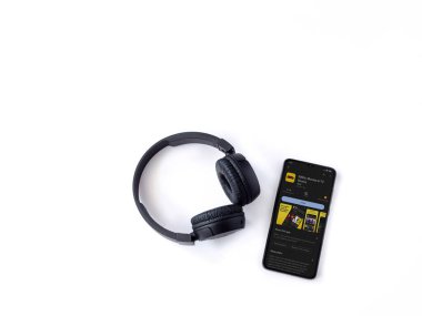 Lod, Israel - July 16,2023: Smartphone with IDMb app play store page and wireless headphones on white background. Top view flat lay with copy space.