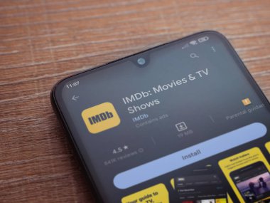 Lod, Israel - July 16,2023: IDMb app play store page on smartphone on wooden background. Top view flat lay with copy space.