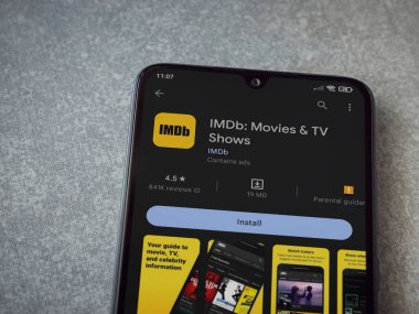 Lod, Israel - July 16,2023: IDMb app play store page on smartphone on ceramic stone background. Top view flat lay with copy space.