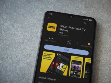 Lod, Israel - July 16,2023: IDMb app play store page on smartphone on ceramic stone background. Top view flat lay with copy space.