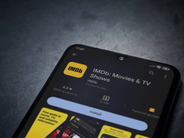 Lod, Israel - July 16,2023: IDMb app play store page on smartphone on a dark marble stone background. Top view flat lay with copy space.