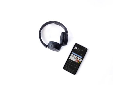 Lod, Israel - July 16,2023: Smartphone with Udemy app play store page and wireless headphones on white background. Top view flat lay with copy space.