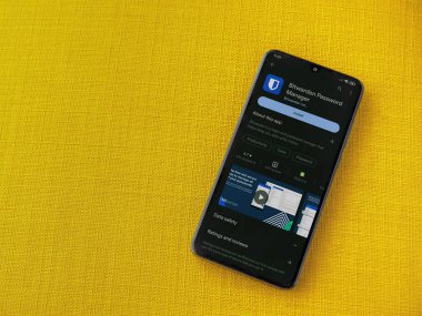Lod, Israel - July 16,2023: Bitwarden Password Manager app play store page on smartphone on a yellow fabric background. Top view flat lay with copy space.