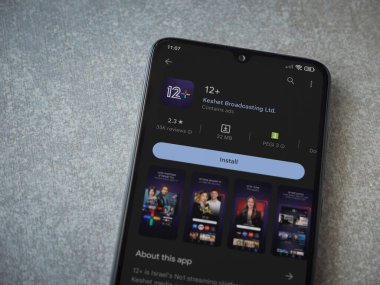 Lod, Israel - July 16,2023: 12+ app play store page on smartphone on ceramic stone background. Top view flat lay with copy space.