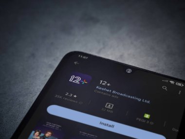 Lod, Israel - July 16,2023: 12+ app play store page on smartphone on a dark marble stone background. Top view flat lay with copy space.