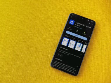 Lod, Israel - 16 Temmuz 2023: Sarı kumaş arka planda akıllı telefon üzerinden sikke bazlı uygulama oyun mağazası sayfası. Üst görünüm düzlüğü kopyalama alanı ile yatıyordu.