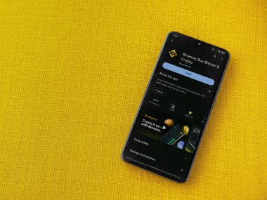 Lod, Israel - 16 Temmuz 2023: Binance uygulama oyun mağazası sayfası sarı kumaş arka planda akıllı telefon. Üst görünüm düzlüğü kopyalama alanı ile yatıyordu.