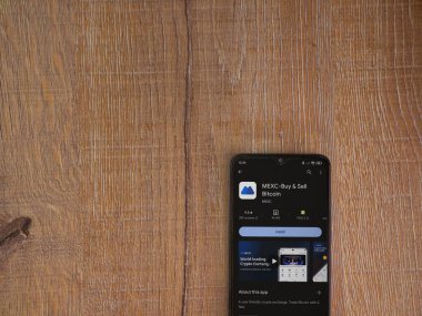 Lod, Israel - 16 Temmuz 2023: MEXC uygulama oyun mağazası sayfası ahşap zemin üzerinde akıllı telefon. Üst görünüm düzlüğü kopyalama alanı ile yatıyordu.