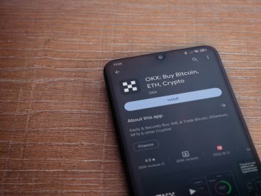 Lod, Israel - 16 Temmuz 2023: OKX uygulama oyun mağazası sayfası ahşap arka planda akıllı telefon. Üst görünüm düzlüğü kopyalama alanı ile yatıyordu.