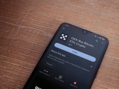Lod, Israel - 16 Temmuz 2023: OKX uygulama oyun mağazası sayfası ahşap arka planda akıllı telefon. Üst görünüm düzlüğü kopyalama alanı ile yatıyordu.
