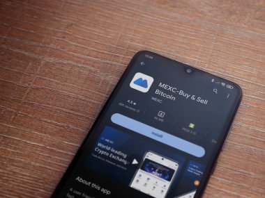 Lod, Israel - 16 Temmuz 2023: MEXC uygulama oyun mağazası sayfası ahşap zemin üzerinde akıllı telefon. Üst görünüm düzlüğü kopyalama alanı ile yatıyordu.