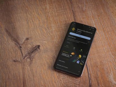 Lod, Israel - 16 Temmuz 2023: Binance uygulama oyun mağazası sayfası ahşap arka planda akıllı telefon. Üst görünüm düzlüğü kopyalama alanı ile yatıyordu.