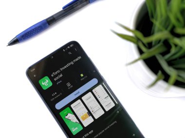 Lod, Israel - 16 Temmuz 2023: Beyaz arka planda eToro uygulamalı akıllı telefonlu modern çalışma alanı. Üst görünüm yatağını kapat.