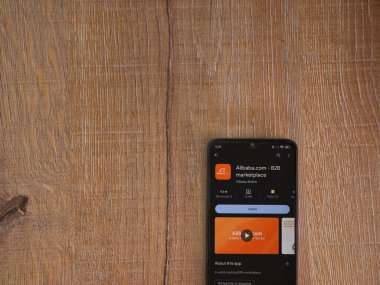 Lod, Israel - 16 Temmuz 2023: Alibaba.com uygulama oyun mağazası sayfası ahşap zemin üzerinde akıllı telefon. Üst görünüm düzlüğü kopyalama alanı ile yatıyordu.