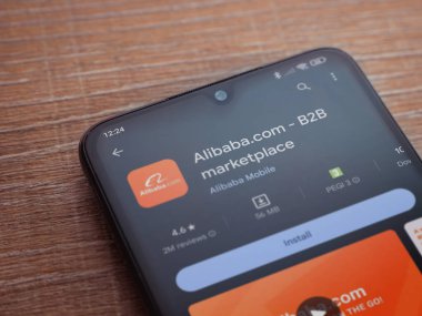 Lod, Israel - 16 Temmuz 2023: Alibaba.com uygulama oyun mağazası sayfası ahşap zemin üzerinde akıllı telefon. Üst görünüm düzlüğü kopyalama alanı ile yatıyordu.